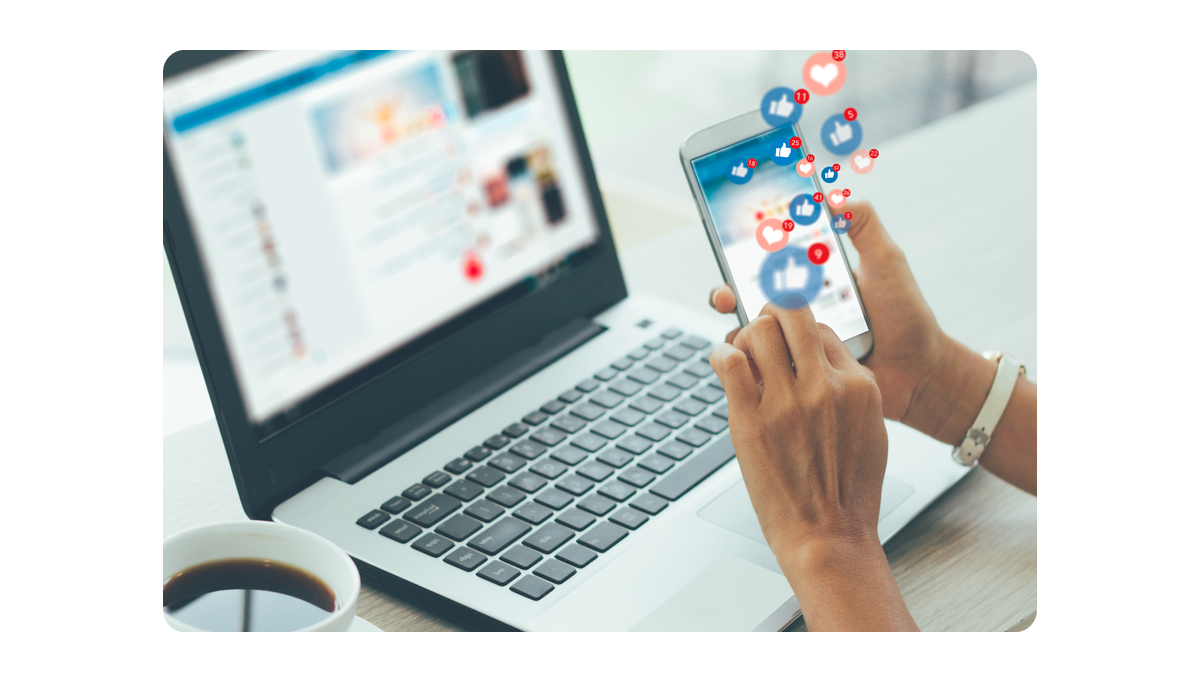 A person using a smartphone with floating social media icons while working on a laptop, symbolizing digital engagement.png