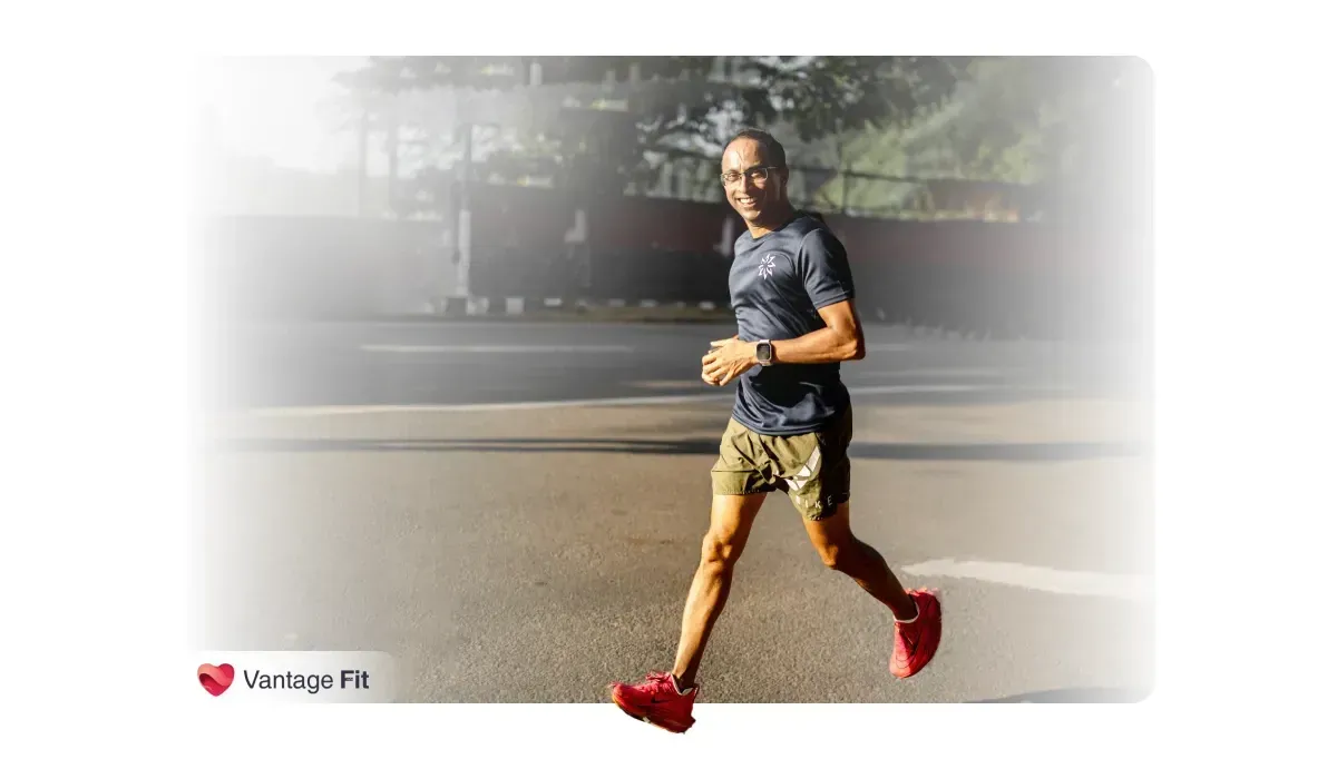 A man jogging outdoors, smiling while wearing a dark blue t-shirt, shorts, and red running shoes, with a watch on his wrist, captured in natural daylight.webp