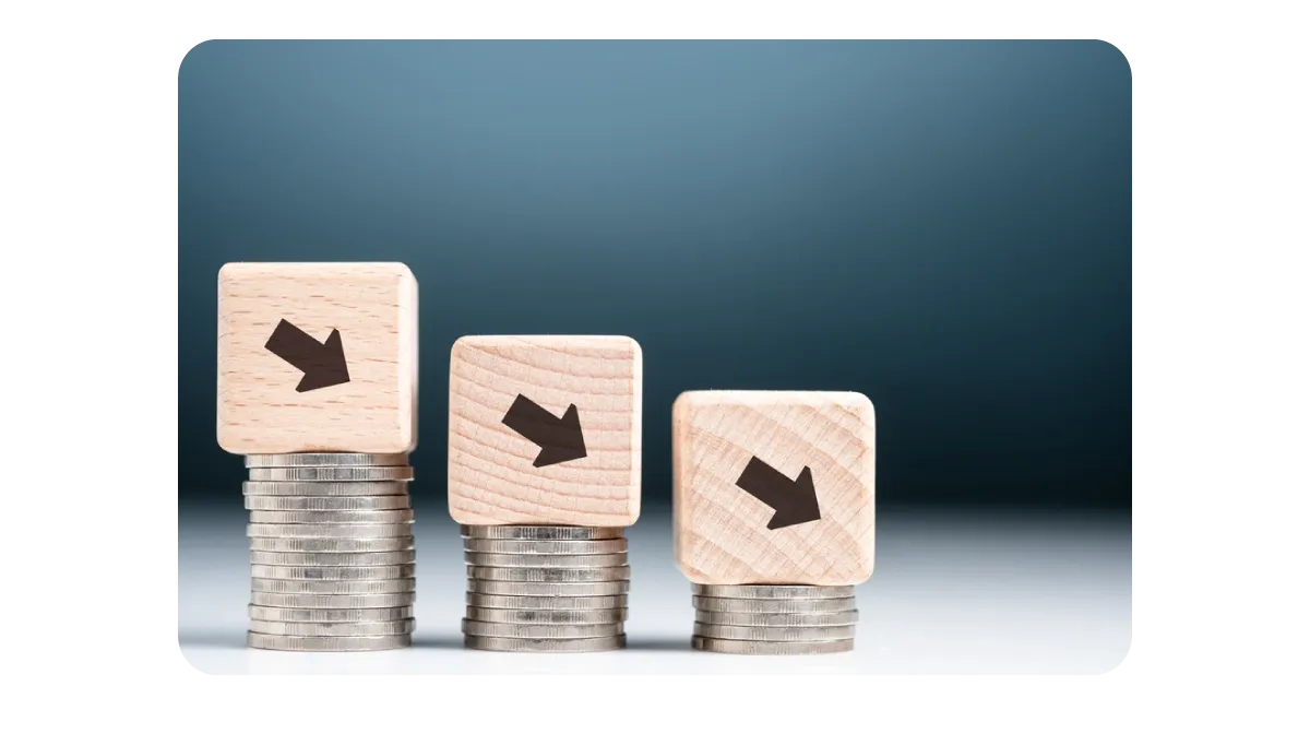 A visual representation of declining financial trends, with wooden blocks featuring downward arrows stacked on top of coins.